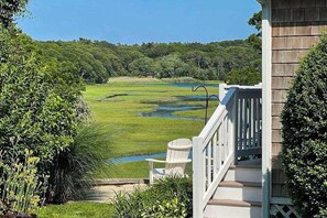 A view from a porch overlooking a grassy area with a small body of water, surrounded by trees.