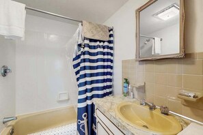 Ein Badezimmer mit einer Badewanne, einem Waschbecken, einem Spiegel und einem gestreiften Duschvorhang.
