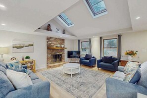 Uma sala de estar ampla com lareira, sofás azuis, uma mesa de centro e claraboias.