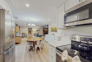 Cozinha moderna com eletrodomésticos de aço inoxidável, sala de jantar com cadeiras brancas e uma ilha central.