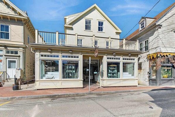 A two-story building with a balcony on the second floor, storefronts on the ground floor, and a clear blue sky above.