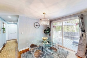 Un coin repas avec une table en verre, des chaises en fil de fer, un lustre et une vue sur une terrasse extérieure.