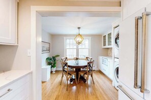 A kitchen with a dining table, chairs, a chandelier, and a washing machine. - Cottage w/ water views from front yard, central ac & fireplace (Vineyard Haven)