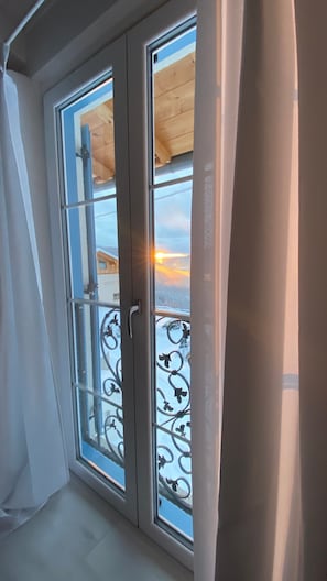 Ein Zimmer mit einem großen Fenster, einem Metallgeländer und Blick auf eine verschneite Landschaft.