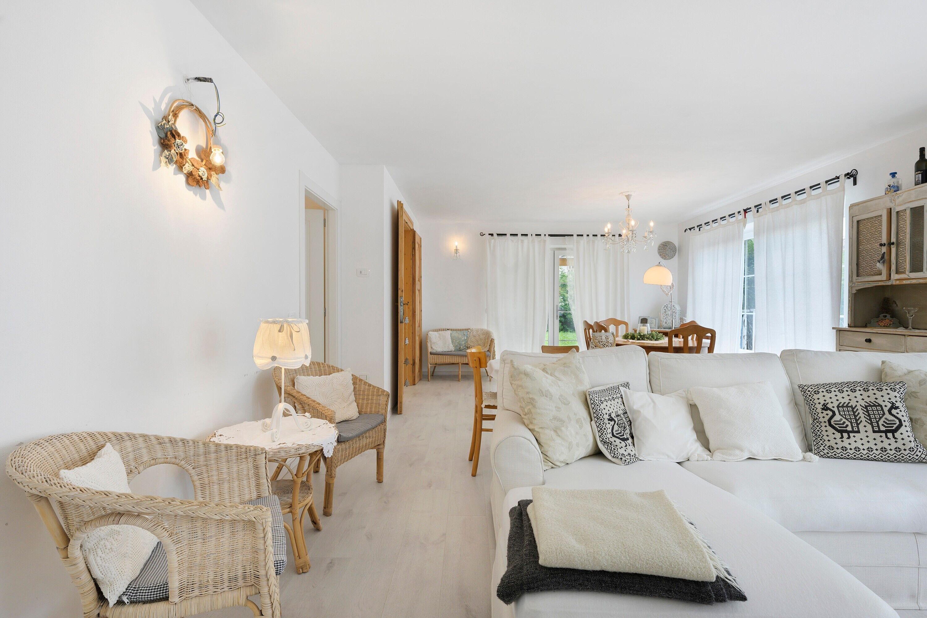 Ein Wohnzimmer mit einem weißen Sofa, Korbstühlen, einem Esstisch und einer Chandelier.