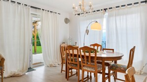 Un comedor con una mesa redonda de madera, seis sillas, una araña y vistas al exterior.
