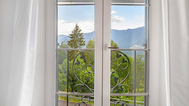 Habitación con un amplio ventanal, barandilla de metal en el balcón y vistas a las montañas.