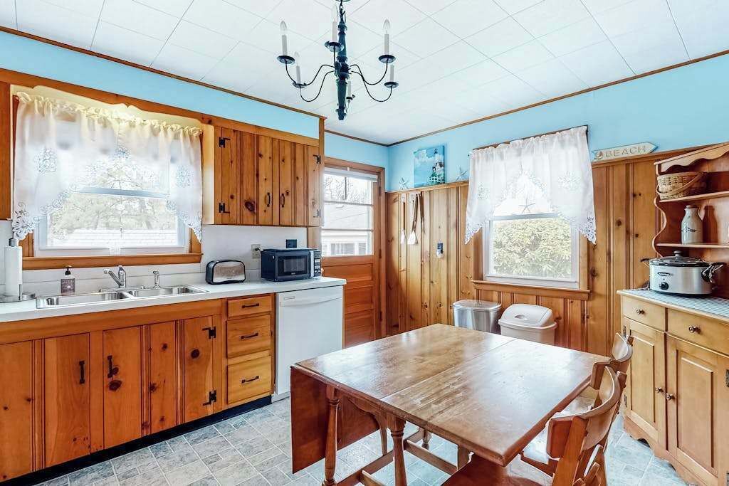 A kitchen with wooden cabinets, a dining table, a chandelier, and a view of the outdoors.