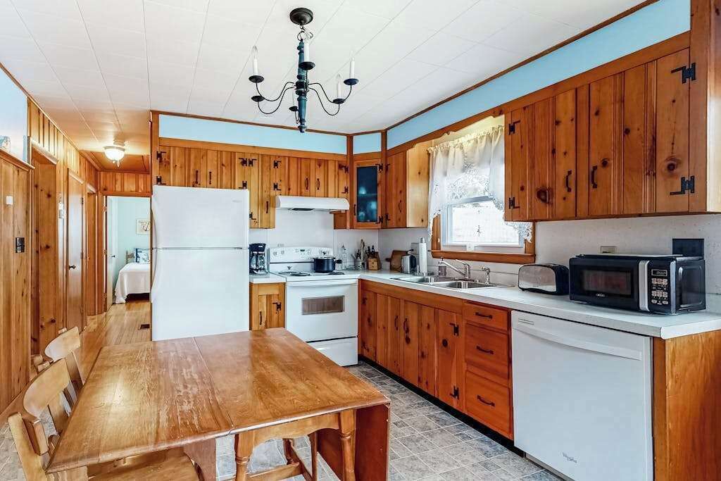 A compact kitchen with wooden cabinets, a dining table, a refrigerator, a stove, and a microwave.