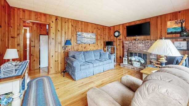 A wooden-paneled room with a sofa, a television, a fireplace, and a clock on the wall. - Cozy cottage, WiFi, A/C, Gas grill, W/D, Firepit (South Yarmouth)