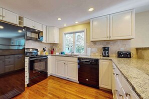 A modern kitchen with white cabinets, a stainless steel refrigerator, a dishwasher, and a window providing natural light. - Classic home with deck, patio & yard - walk to Cockle Cove & Forest Beaches (South Chatham)