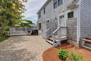 A house with a paved patio, a wooden deck, and a small garden area. - Classic home with deck, patio & yard - walk to Cockle Cove & Forest Beaches (South Chatham)
