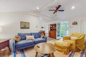 A living room with a blue sofa, a yellow armchair, a wooden coffee table, and a ceiling fan.