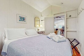 A bedroom with a bed, a mirror, a framed picture, and a view into the kitchen.