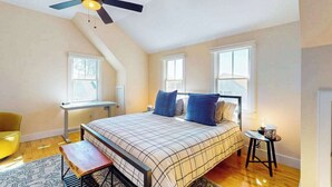 Ein Schlafzimmer mit Bett, Schreibtisch, Stuhl, Deckenventilator und Fenster.