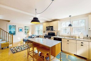 A modern kitchen with a central island, wooden flooring, and large windows. - Charming condo with parking, washer/dryer, AC, and deck (Provincetown)