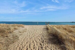 Een zandpad langs het strand dat naar de oceaan leidt, met een houten omheining aan de ene kant en een helderblauwe lucht.