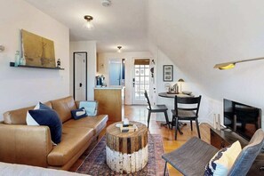 A living room with a sofa, coffee table, TV, and a dining area with chairs and a table. - Cozy condo in great location with deck, board games, & AC (Provincetown)