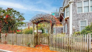 Un quartier résidentiel avec une clôture en bois, un chemin pavé de briques et une maison dotée d’un balcon.