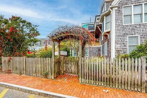 A residential area with a wooden fence, a brick pathway, and a house with a balcony. - Light-filled home near beach and shops with AC, W/D, & balcony (Provincetown)