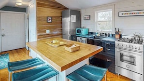 Une cuisine avec des éléments en bois, un îlot central, des tabourets de bar, une cuisinière et un four à micro-ondes.