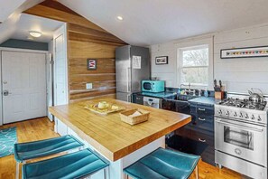 A kitchen with wooden accents, a central island, bar stools, a stove, and a microwave. - Light-filled home near beach and shops with AC, W/D, & balcony (Provincetown)