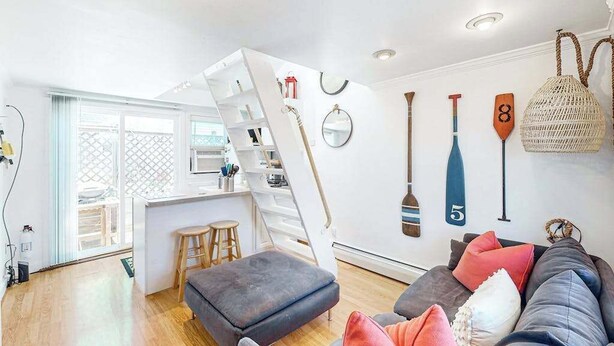 Un espace de vie moderne comprenant un lit en mezzanine, un coin cuisine et un espace détente avec des coussins.