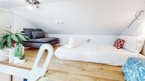 Une chambre de style loft moderne avec un plafond en pente, un lit avec une literie blanche, un canapé foncé, une chaise blanche et une petite table agrémentée de plantes.