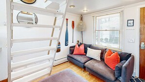 Un salon avec un canapé gris, des coussins orange, une échelle blanche et une lampe suspendue.