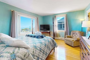 Quarto com cama, televisão, poltrona e cômoda.