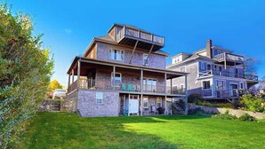 A multi-story residential building with a covered porch, a stone foundation, and a grassy yard.