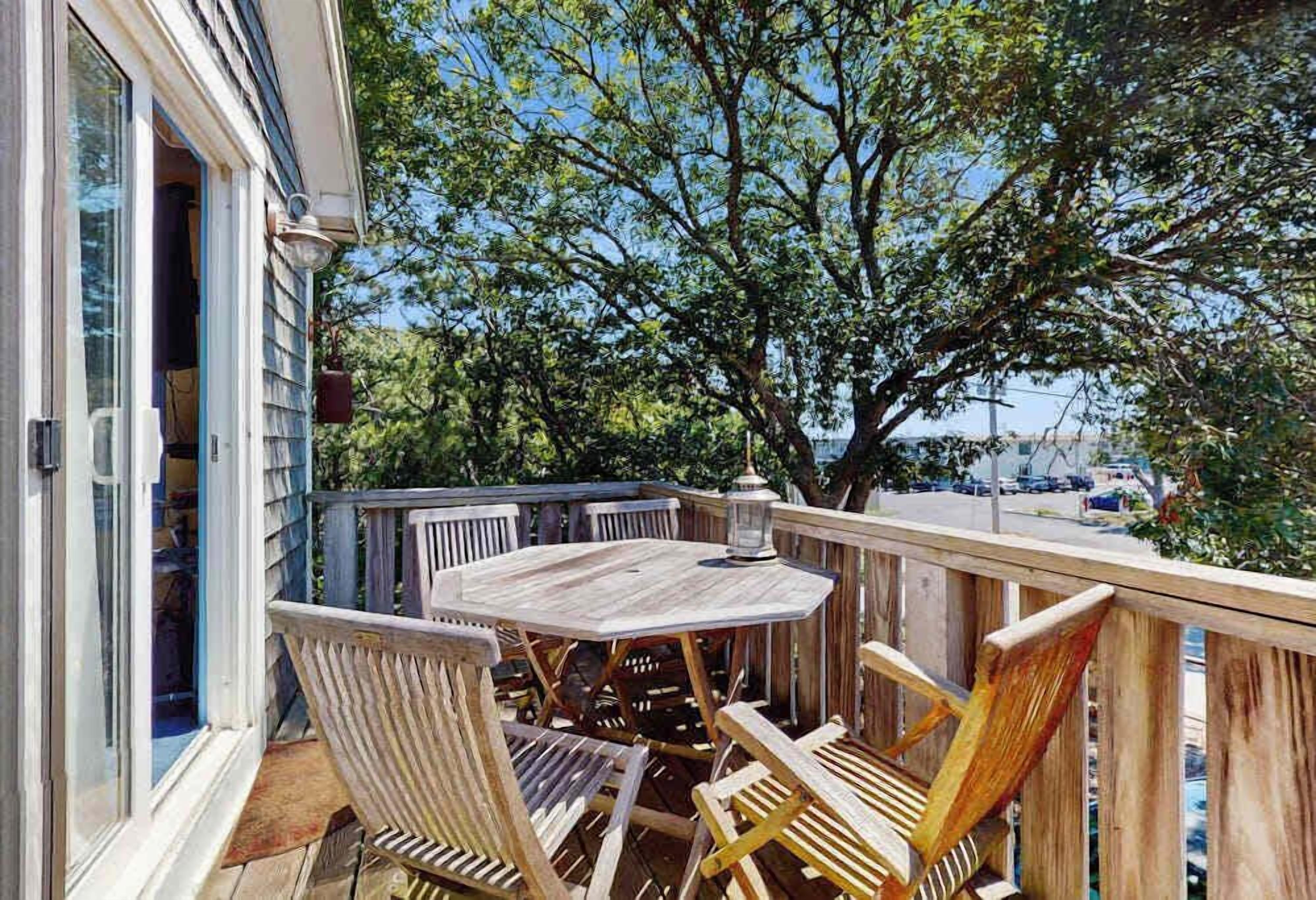 A wooden deck with a round table and chairs, a lantern, and a view of a tree and a building.