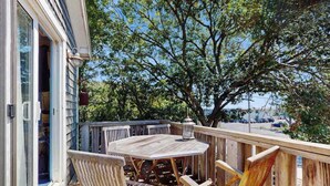Eine Holzterrasse mit rundem Tisch und Stühlen, einer Laterne und Blick auf einen Baum und ein Gebäude.