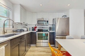 A modern kitchen with white cabinets, stainless steel appliances, a built-in oven, and a microwave. - Second-floor condo steps from downtown with large deck, partial bay view & AC (Provincetown)