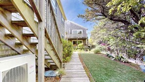 A residential building with a wooden deck, a lawn, and a garden with various plants. - Cheerful condo with enclosed porch, next to Cape Cod Bay with beach access (Provincetown)