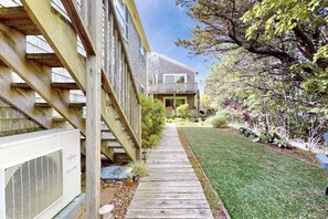 A residential building with a wooden deck, a lawn, and a garden with various plants. - Cheerful condo with enclosed porch, next to Cape Cod Bay with beach access (Provincetown)