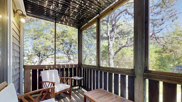 A covered outdoor seating area with wooden furniture and large windows. - Cheerful condo with enclosed porch, next to Cape Cod Bay with beach access (Provincetown)