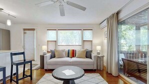 A modern living room with a sofa, a coffee table, a ceiling fan, and large windows. - Cheerful condo with enclosed porch, next to Cape Cod Bay with beach access (Provincetown)