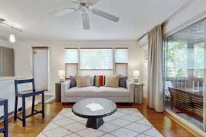 A modern living room with a sofa, a coffee table, a ceiling fan, and large windows. - Cheerful condo with enclosed porch, next to Cape Cod Bay with beach access (Provincetown)