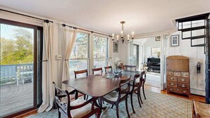 Un espace repas comprenant une grande table, des chaises, un lustre et une vue sur l’extérieur grâce aux portes vitrées.