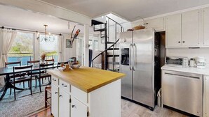 Une cuisine moderne dotée d’un îlot central, d’appareils électroménagers en acier inoxydable et d’un escalier menant à un niveau supérieur.
