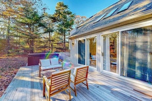 Eine Holzterrasse mit Sitzgelegenheiten im Freien, einem Whirlpool und einem überdachten Glasbalkon.