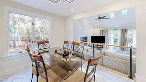 Un'area pranzo moderna con un tavolo in vetro, sedie in legno e una TV sullo sfondo.