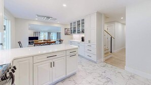 Una cucina moderna con mobili bianchi, un piano di lavoro in marmo e una zona pranzo con tavolo e sedie.