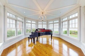 A grand room with a piano, large windows, and a chandelier.