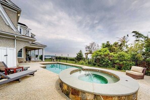 A swimming pool with a hot tub, lounge chairs, and a house with a balcony.