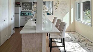 A kitchen with a marble countertop, white cabinets, and a dining area with a white table and chairs. - Lakefront home with private dock, deck, & lovely view - short drive to the cape (Plymouth)