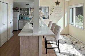 A kitchen with a marble countertop, white cabinets, and a dining area with a white table and chairs.