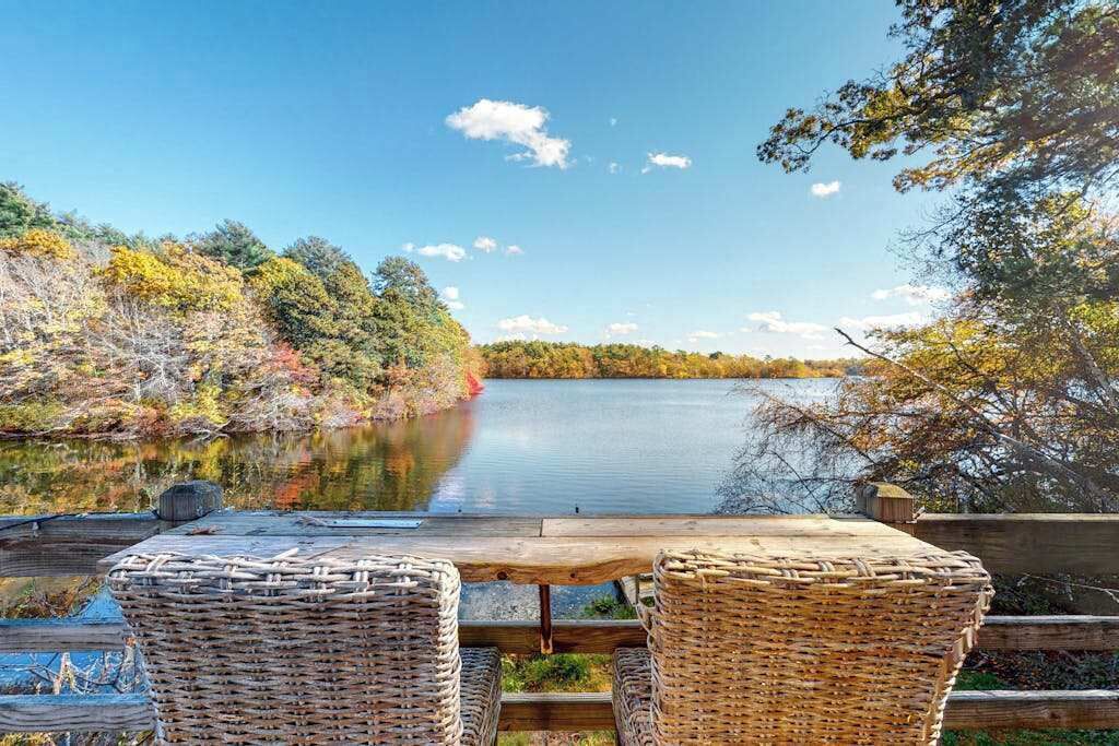 A wooden deck with wicker chairs overlooking a lake, surrounded by trees.