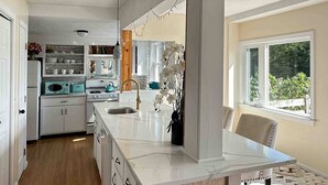 A kitchen with white cabinets, a marble countertop, a sink, and a window with a view of greenery. - Lakefront home with private dock, deck, & lovely view - short drive to the cape (Plymouth)